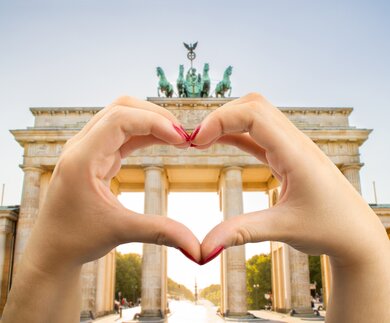 Herz vor Brandenburger Tor in Berlin  | © Gettyimages.com/Manuel-F-O Hande mit rot lackierten Fingernägeln formen ein Herz vor dem Brandenburger Tor in Berlin  | © Gettyimages.com/Manuel-F-O
