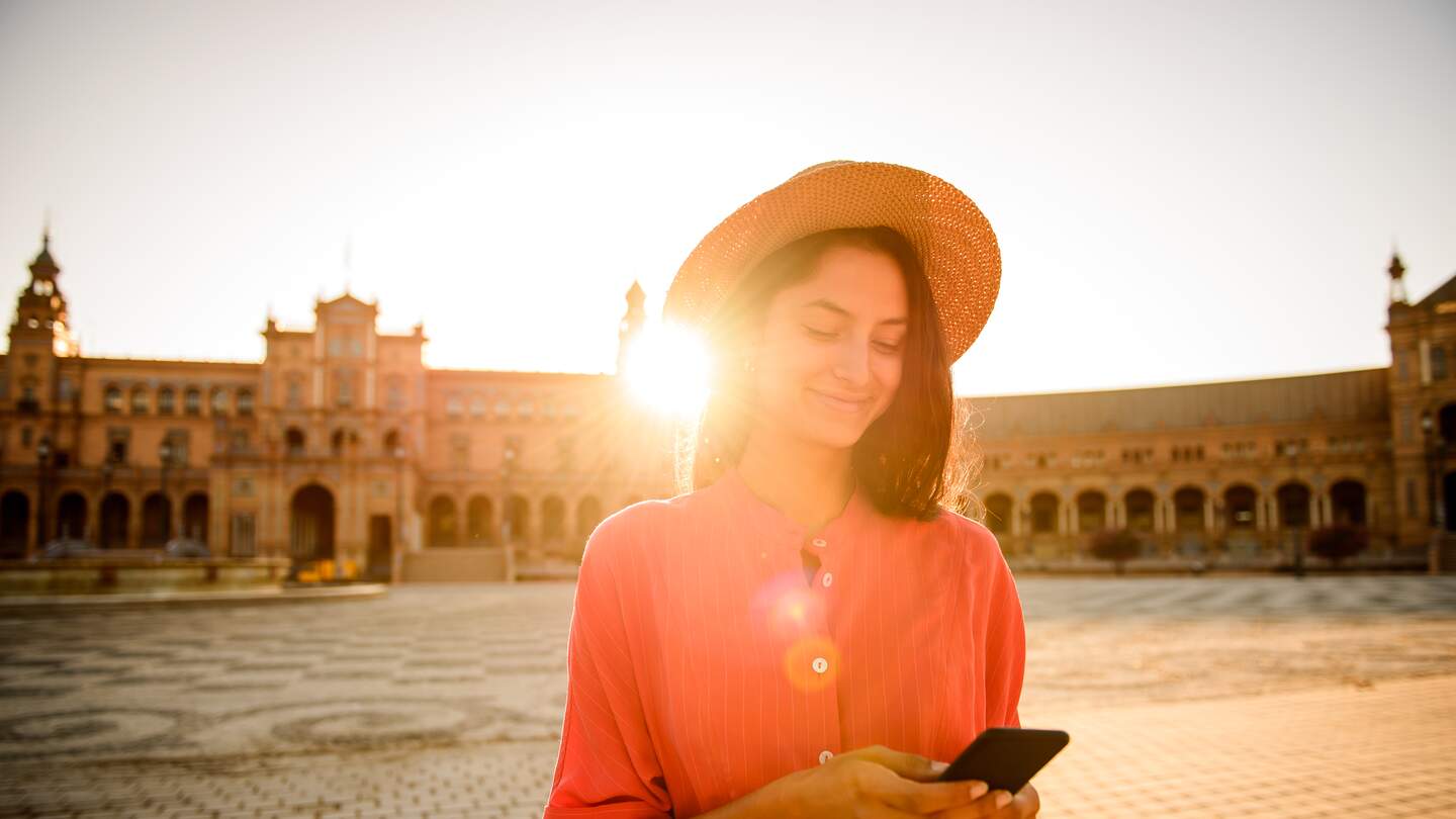 Elegante Frau mit Mobiltelefon in der Hand | © gettyimages.com/MStudioimages Elegante Frau beim Besuch der Plaza de Espana, Sevilla mit Handy in der Hand | © gettyimages.com/MStudioimages