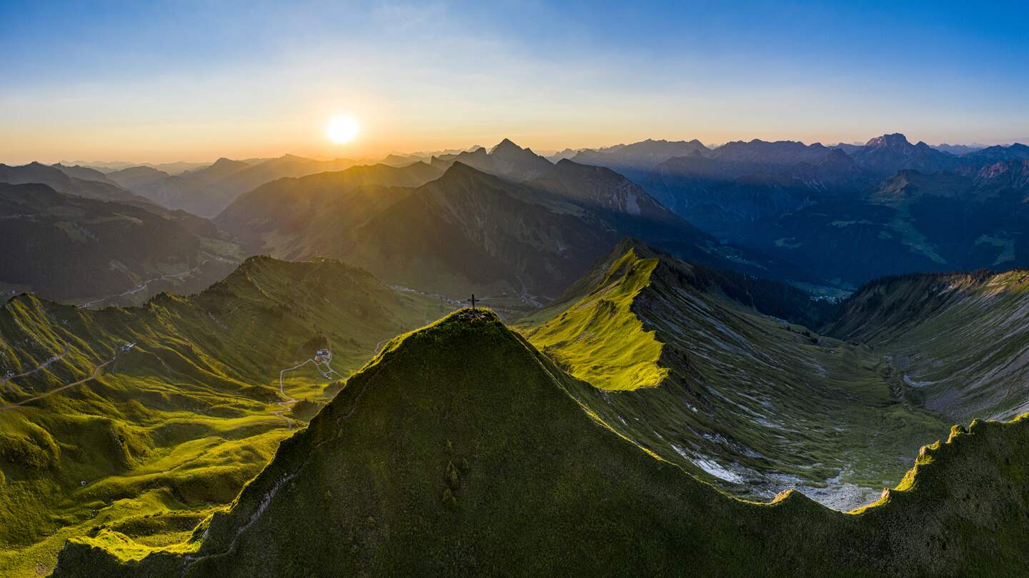 Luftaufnahme des Sonnenaufgangs auf dem Glatthorn (2133m) in Vorarlberg, dem westlichsten Teil Österreichs. Auf dem Gipfel des Berges liegen ein paar anonyme Menschen in ihren Schlafsäcken. | © Gettyimages.com/kemter