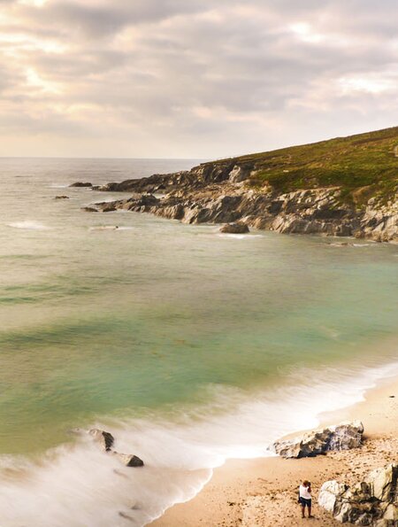 Strand und Steine in Corwall, England | ©  aliciafabregas / 2016 Thinkstock. Panoramaansicht einer Küstenszene in Cornwall, England, mit einem Sandstrand, zerklüfteten Klippen und einer grasbewachsenen Landzunge | ©  aliciafabregas / 2016 Thinkstock.