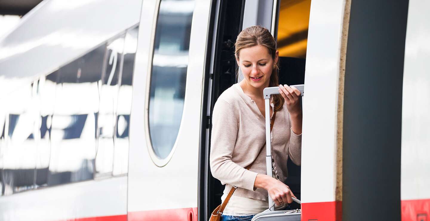 Bahnsteig | © Gettyimages.com/ViktorCap Eine Frau steht an der Tuer eines rotgestreiften Zuges. | © Gettyimages.com/ViktorCap