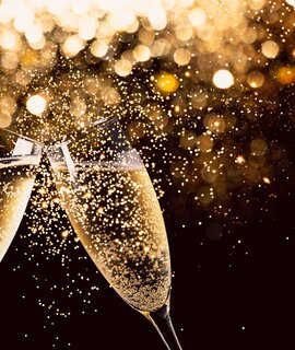 Glaeser Champagner stossen in der Nacht  | © Gettyimages.com/ASIFE zwei Glaeser Champagner stossen in der Nacht mit Lichtern im  Glitzer und Funken im Hintergrund an | © Gettyimages.com/ASIFE