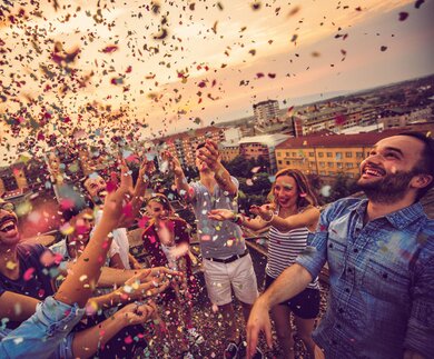 Freunde auf Dachterrasse mit Konfetti | © Gettyimages.com/AleksandarNakic Freundesgruppe schmeißt auf Dachterrasse buntes Konfetti in den Himmel | © Gettyimages.com/AleksandarNakic