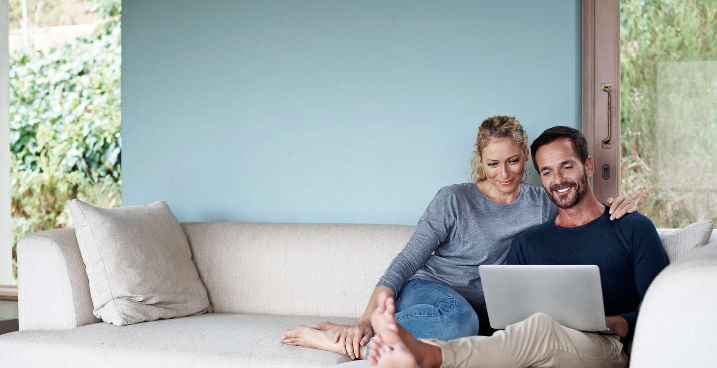 Paar auf dem Sofa | © kupicoo/GettyImages Ganzkoerperaufnahme eines Paares, das einen Laptop benutzt, während es sich auf dem Sofa entspannt | © kupicoo/GettyImages
