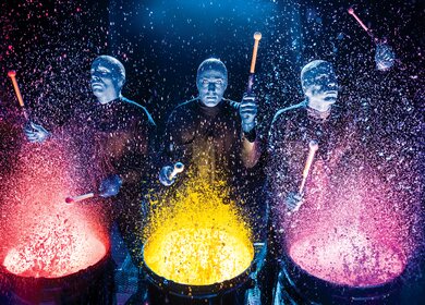 Die Blue Man Group spielt auf Farbtrommeln, Farbe spritzt durch die Gegend | © Stage Entertainment