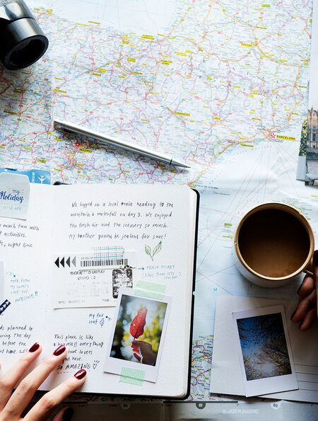 reiseblog_bullethournal_reiseplanung | © gettyimages.com/Rawpixel Ltd. eine flache Anordnung verschiedener Reiseutensilien auf einer Oberflaeche, darunter eine Karte, ein Fernglas, ein Reisepass, Postkarten, Fotos und eine Tasse Kaffee | © gettyimages.com/Rawpixel Ltd.