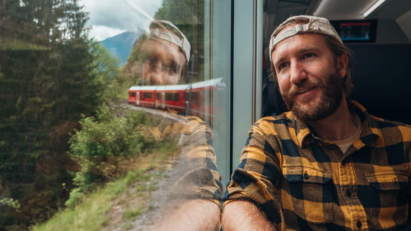 Mann sitzt am Zugfenster und schaut in die vorbeiziehende Landschaft | © gettyimages.com