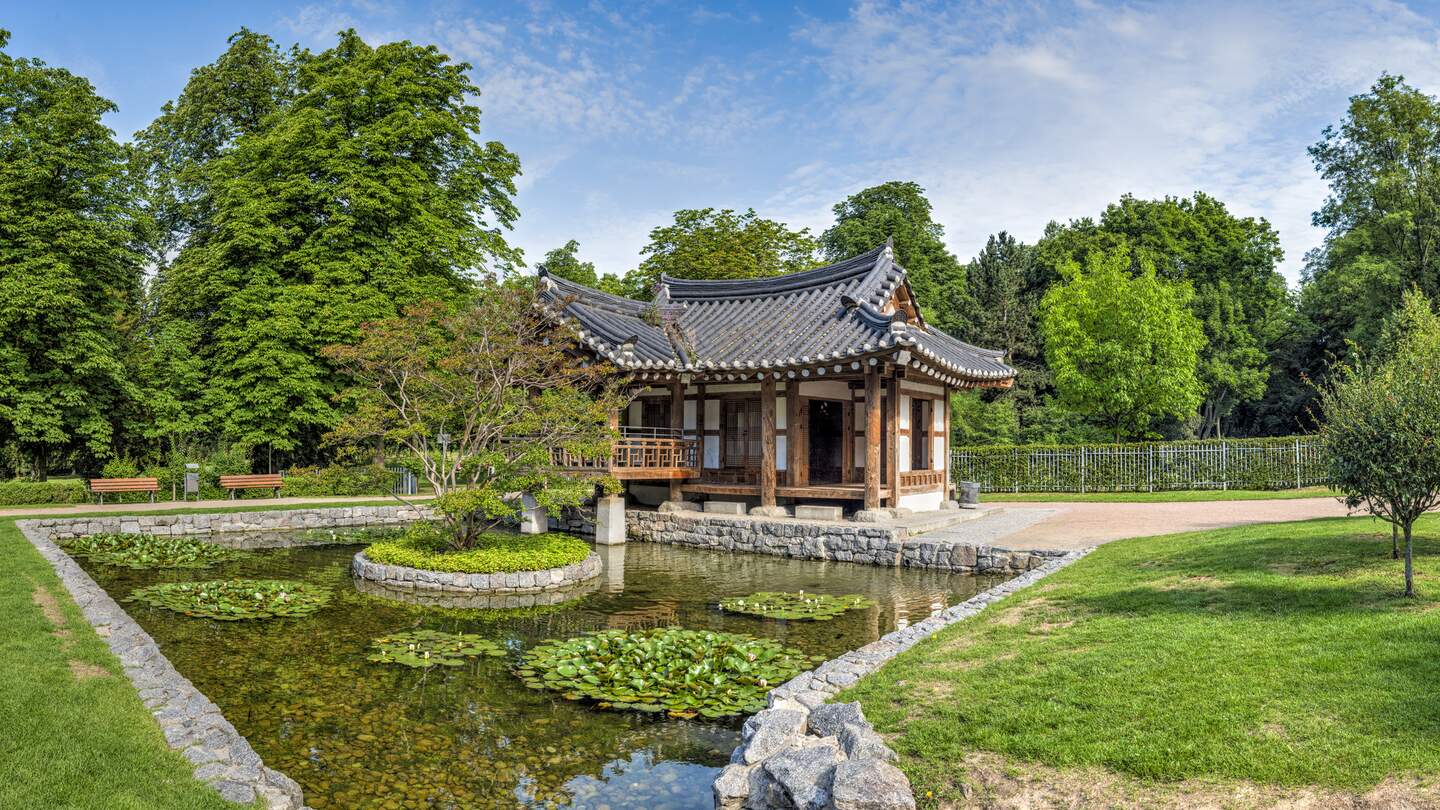 Eine buddhistische Tempelanlage im Grüneburgpark mit typisch asiatischer Architektur bei Sommerwetter und einem Teich im Vordergrund | © Gettyimages.com/Frank Wagner