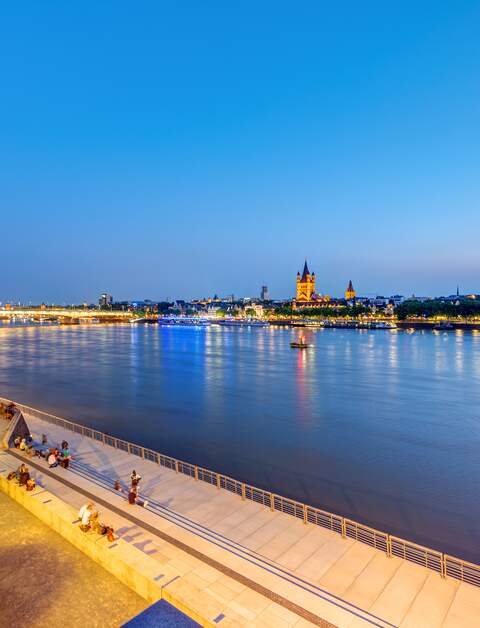Menschen sitzen am Rheinufer in Köln nach Sonnenuntergang. | © Gettyimages.com/elxeneize