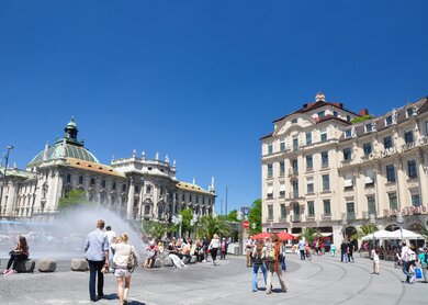 Karlsplatz mit Justizpalast in Müchen im Sommer mit Wasserfontänen und vielen Touristen | © Gettyimages.com/wallix