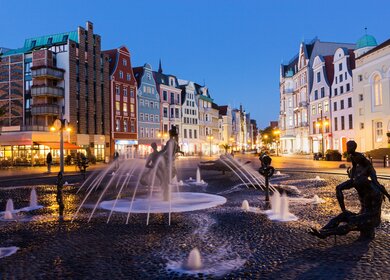 Blick auf den Marktplatz in Rostock mit einem Brunnen am Abend | © Gettyimages.com/prosiaczeq