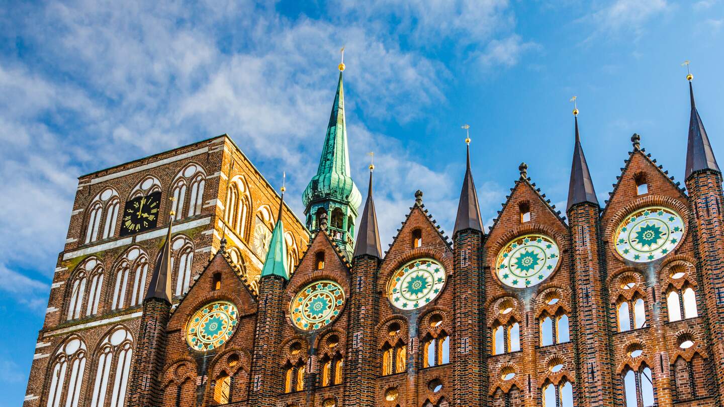 Fassade des historischen Rathauses in Stralsund im Stil der norddeutschen Backsteingotik mit der Nikolaikirche im Hintergrund | © Gettyimages.com/A-Tom