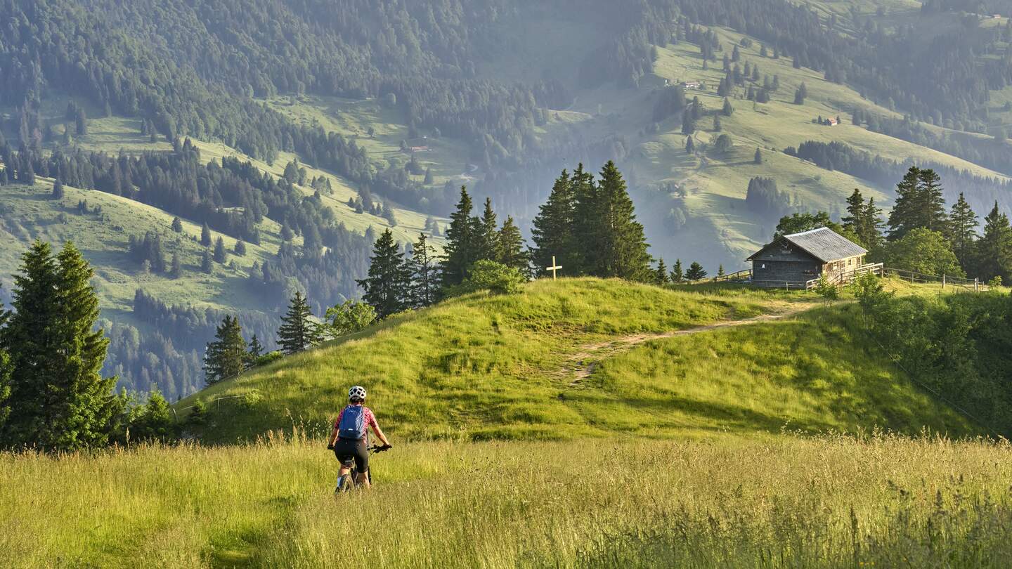 Frau fährt ihr Elektro-Mountainbike in den Bergen oberhalb von Oberstaufen mit Nagelfluh-Bergkette im Hintergrund, Allgäuer Alpen | © Gettyimages.com/Uwe Moser