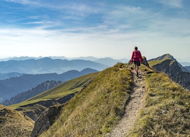 Eine ältere Frau wandert im Herbst auf dem Grat der Nagelfluhkette bei Oberstaufen im Allgäu, Bayern, Deutschland, mit dem Hochgrats-Gipfel im Hintergrund. | © Gettyimages.com/Uwe Moser