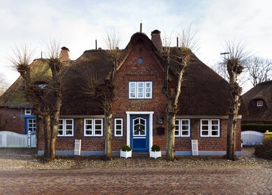 Friesisches Reetdachhaus hinter einer gepflasterten Straße in Nieblum auf Föhr, Schleswig-Holstein | © © Gettyimages.com/eyewave