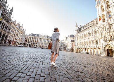 Junge Frau, die auf dem Hauptplatz mit Rathaus in der Altstadt von Brüssel spazieren geht | © Gettyimages.com/RossHelen