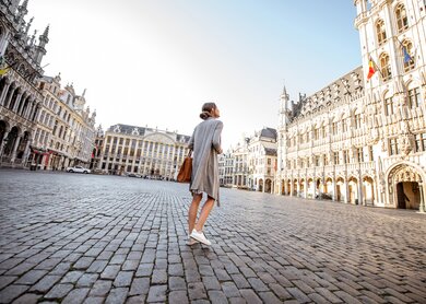 Junge Frau, die auf dem Hauptplatz mit Rathaus in der Altstadt von Brüssel spazieren geht | © Gettyimages.com/RossHelen