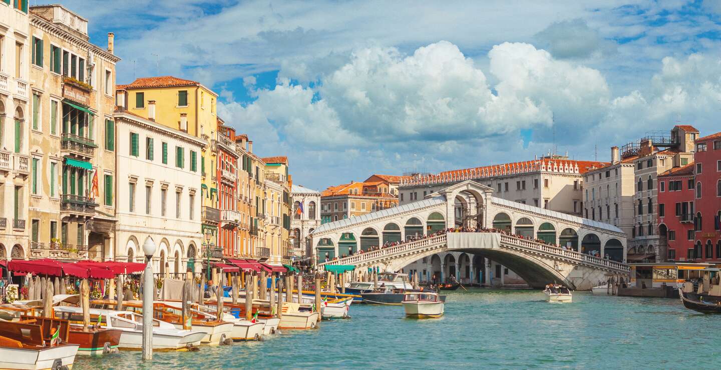 Im Hintergrund die Rialtobrücke mit Touristen, im Vordergrund anliegende Boote auf dem Canal Grande in Venedig. | © Gettyimages.com/mammuth