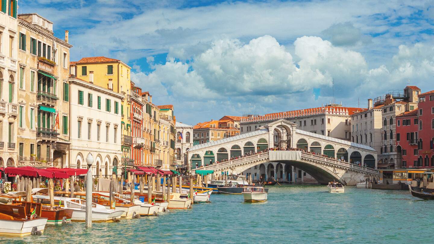 Im Hintergrund die Rialtobrücke mit Touristen, im Vordergrund anliegende Boote auf dem Canal Grande in Venedig. | © Gettyimages.com/mammuth