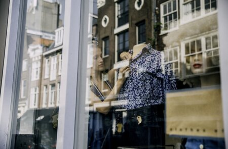 Junge Schaufenster-Dekorateurin in Amsterdam fixiert eine gemusterte Bluse auf einer Büste | © Gettyimages.com/SolStock