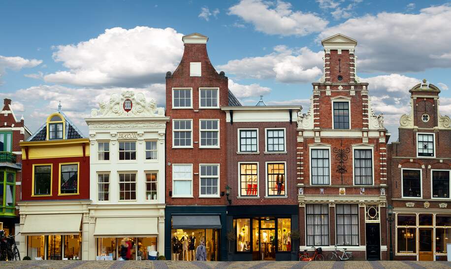 Stadtszene Amsterdam mit liebevoll restaurierten Giebelhäusern und kleinen Ladengeschäften an einer Grachtenbrücke | © Gettyimages.com/MediaProduction