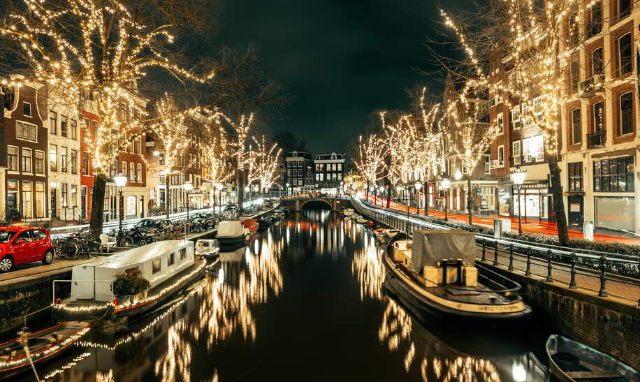 Amsterdam Gracht bei Nacht mit festlichen Weihnachtslichtern in den Bäumen und Spiegelung in der Gracht | © Gettyimages.com/Anton Abramov