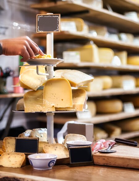 Eine Frau probiert und wählt Bio-Käse von einer Etagere aus vielen Käsesorten in einem Käsegeschäft mit in Amsterdam  | © Gettyimages.com/guruXOOX