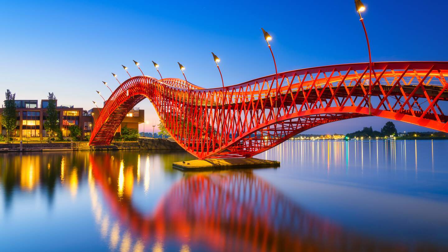 Die abendlich kunstvoll beleuchtete Fußgängerbrücke Python Bridge, auch High Bridge genannt, in Amsterdam spiegelt sich im Kanal | © Gettyimages.com/Biletskiy_Evgeniy