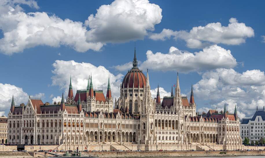 Schrägansicht der Aussenfassade des ungarischen Parlamentsgebäudes in Budapest an der Donau mit blauem Himmel und Schönwetterwolken | © GettyImages.com/Frank Wagner