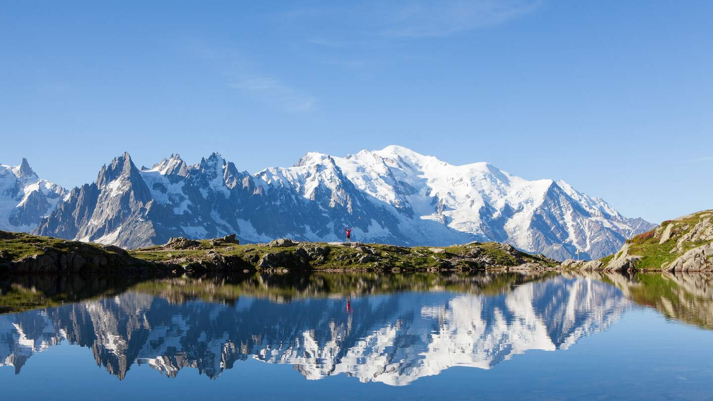 Ein Trailrunner in Rot läuft an einem kristallklaren See entlang, mit dem majestätischen Mont Blanc im Hintergrund. Im Wasser des Sees zeigt sich eine nahezu perfekte Spiegelung. | © Gettyimages.com/nattrass