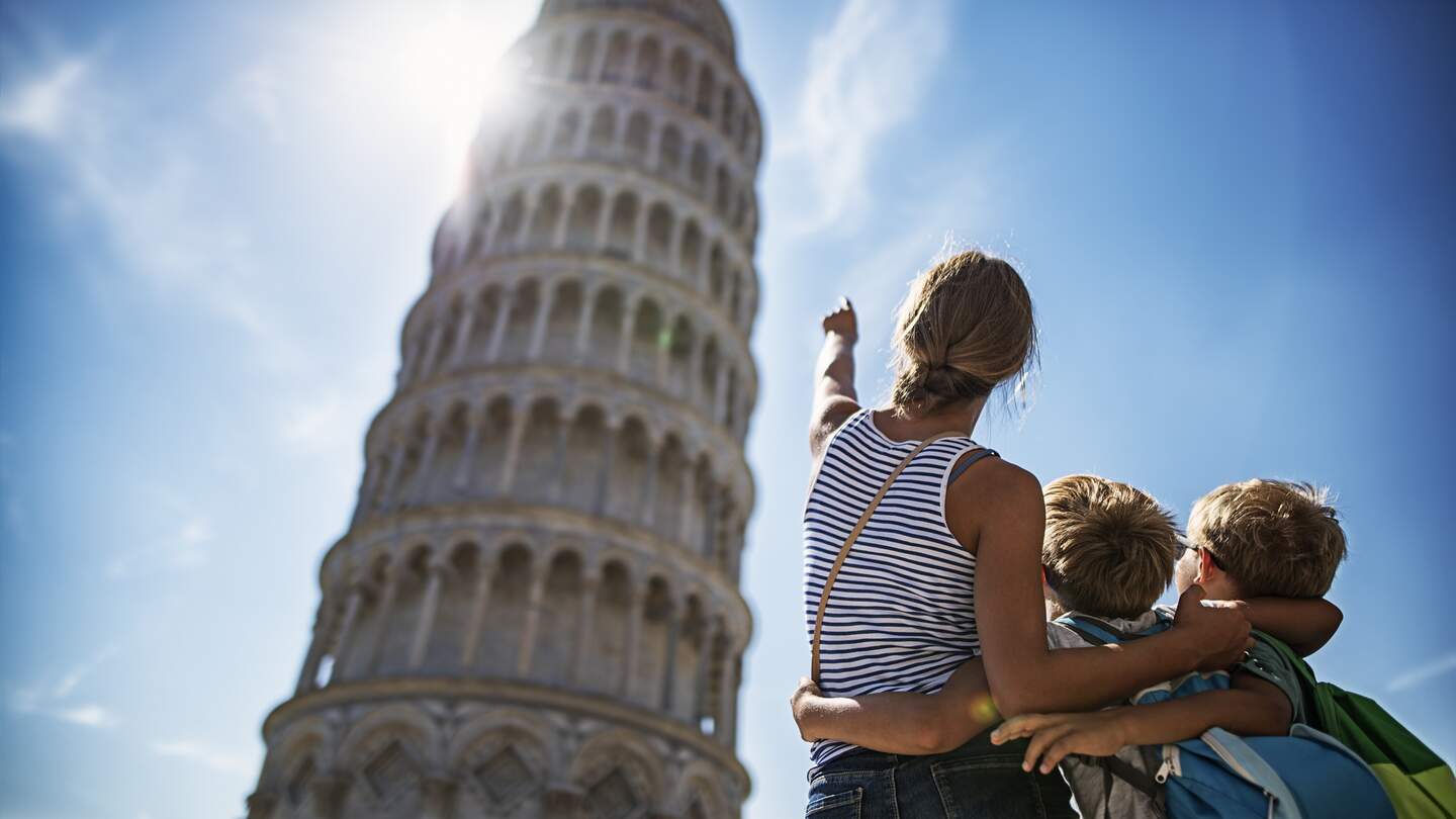 Touristenkinder bei der Besichtigung von Pisa, Italien. Brüder und Schwester stehen auf der Piazza del Miracoli und bewundern den berühmten schiefen Turm von Pisa. | © Gettyimages.com/imgorthand