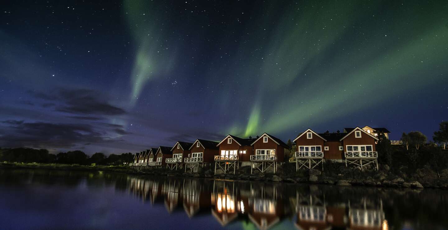 Polarlichter, reflektiert im ruhigen Gewässer, über den roten Hütten in Nordnorwegen | © © Gettyimages.com/Glenn Pettersen