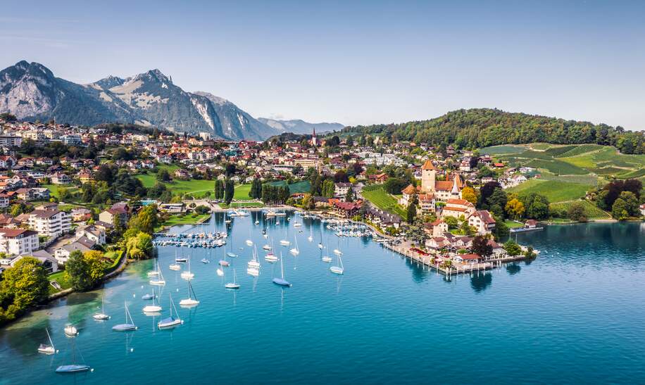 Blick auf den Thuner See, im Hintergrund ist ein Dorf und dahinter Berge. Das Schloss Spiez ist zu sehen. | © Gettyimages.com/JaCZhou