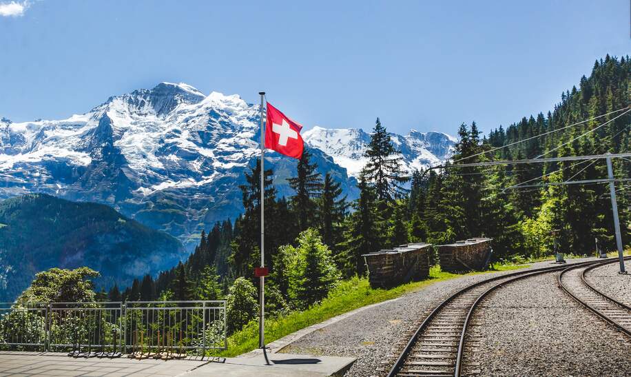 Die Flagge der Schweiz flattert mit der Eisenbahn und dem Berg Jungfrau im Hintergrund. | © gettyimages.com/possawat