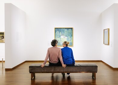 Das Paar sitzt auf einer Bank im Museum und guckt sich ein Gemälde an | ©  Leopold Museum, Wien