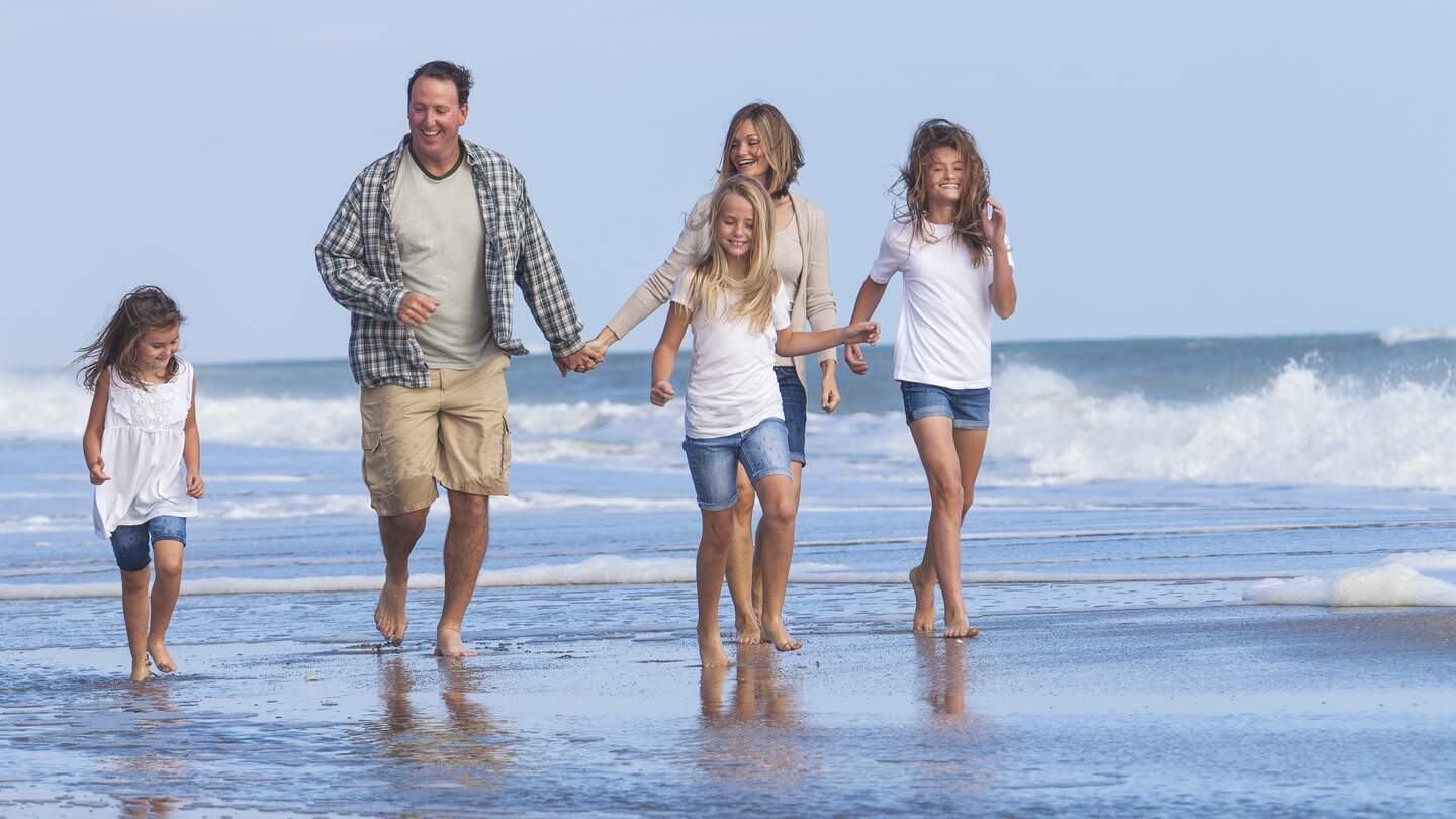 Eltern gehen mit ihren drei Töchtern am Strand spazieren | © Gettyimages.com/Spotmatik