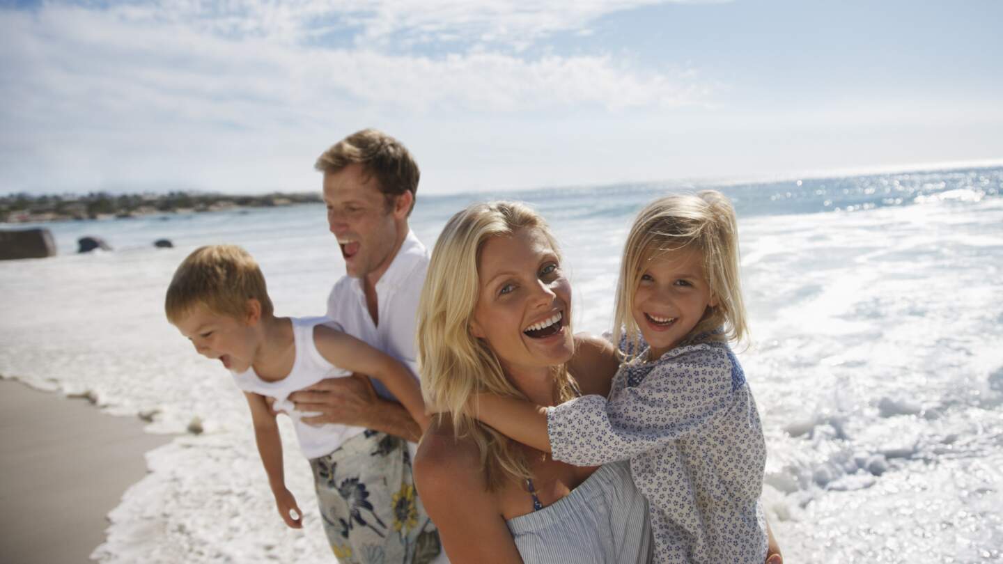 Die Eltern halten ihre Kinder im Arm und lachen am Strand | © Gettyimages.com/Tom Merton