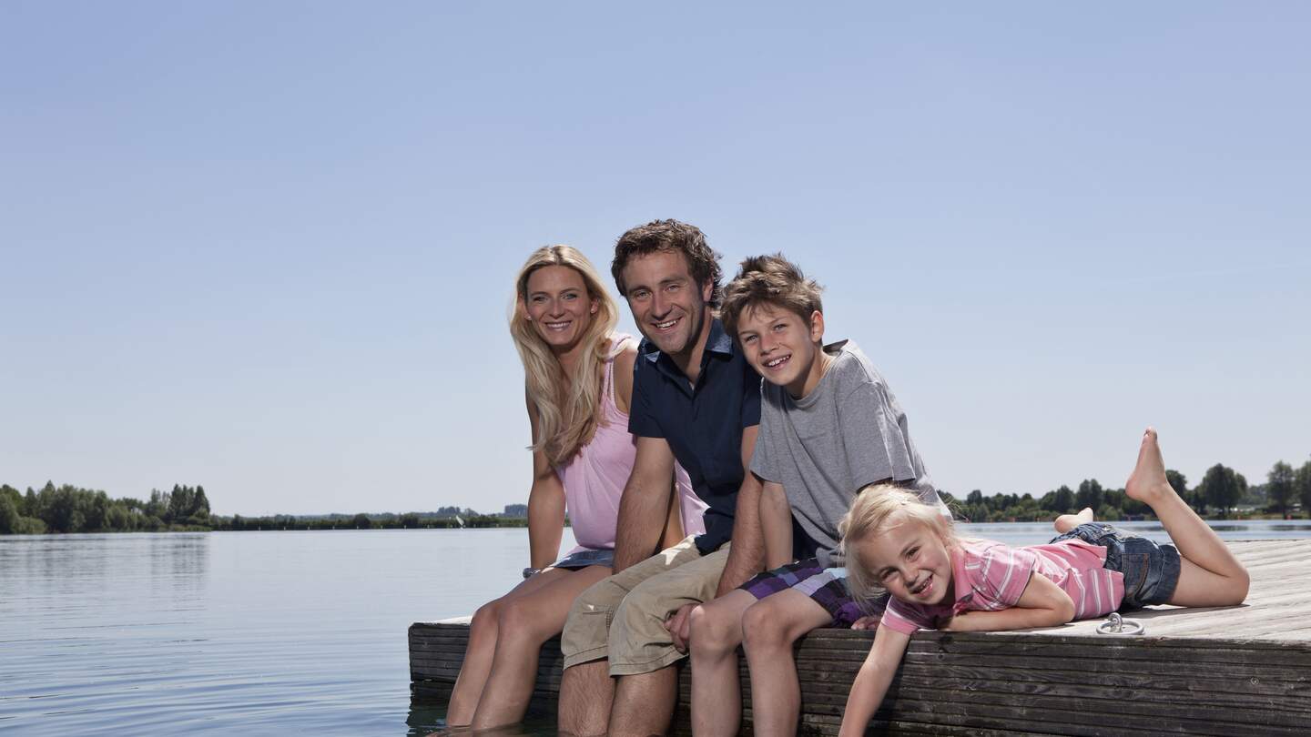 Familie sitzt auf einem Steg und lässt die Füße in den See hängen | © Gettyimages.com/Johnny Valley