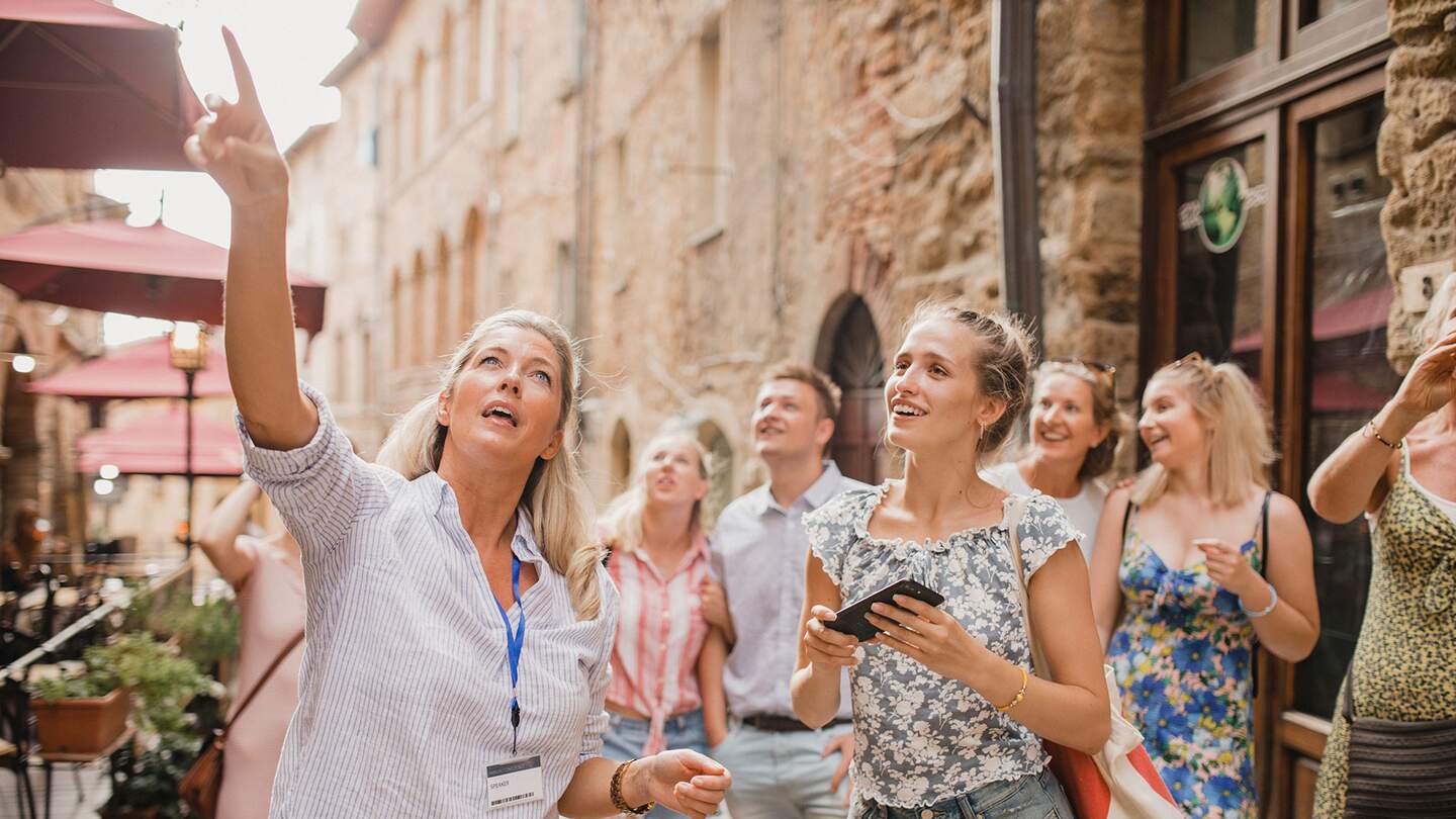 Kleine Reisegruppe auf historischem Stadtrundgang. Sie hört einem Reiseleiter zu, der über die Architektur und die Geschichte spricht. | © Gettyimages.com/SolStock