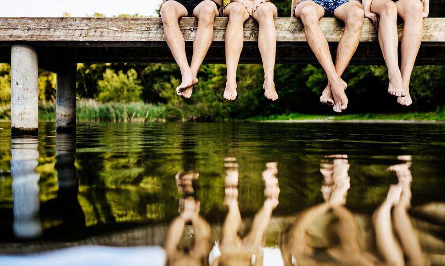 Gruppe von Freunden baumeln mit den  Beinen am Steg über dem See | © Gettyimages.com/TommL