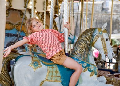 Lächelndes Mädchen auf einem Pferd eines alten Vintage-Karussells in Frankreich | © Gettyimages.com/romrodinka