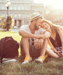 Junges Touristenpaar, das eine fremde Stadt erkundet. Im Park auf Gras sitzen und die Karte auf dem Smartphone ueberpruefen. Tragen Sie Freizeitkleidung und Rucksaecke. Genießen Sie den schoenen sonnigen Tag. | © Gettyimages.com/svetikd