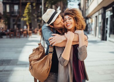 Ein glückliches, junges Paar umarmt sich auf einem Platz vor einem Staßencafe | © Gettyimages.com/Geber86