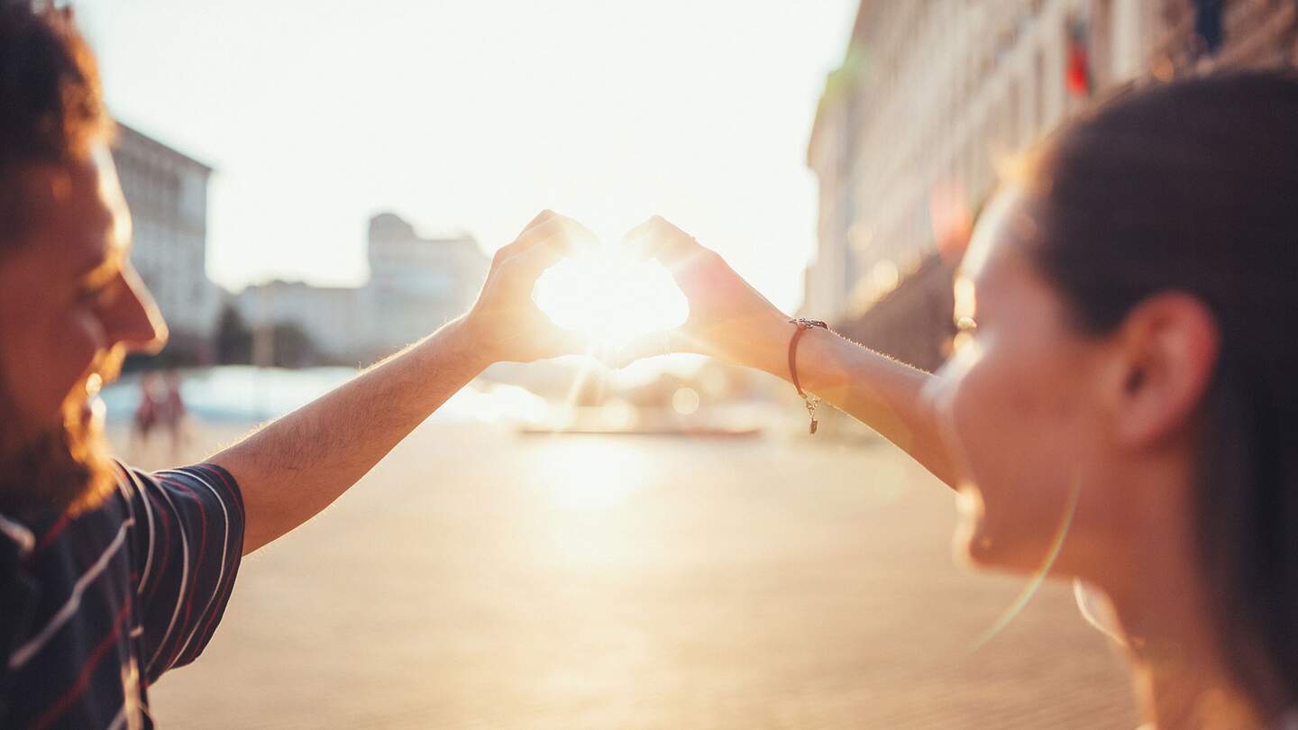 Junges Paar zeigt gemeinsam den Umriss eines Herz-Symbols gegen die untergehende Sonne | © Gettyimages.com/martin-dm