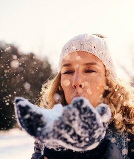 Frau im Freien im Winter pustet Schnee in die Luft | © Gettyimages.com/vgajic