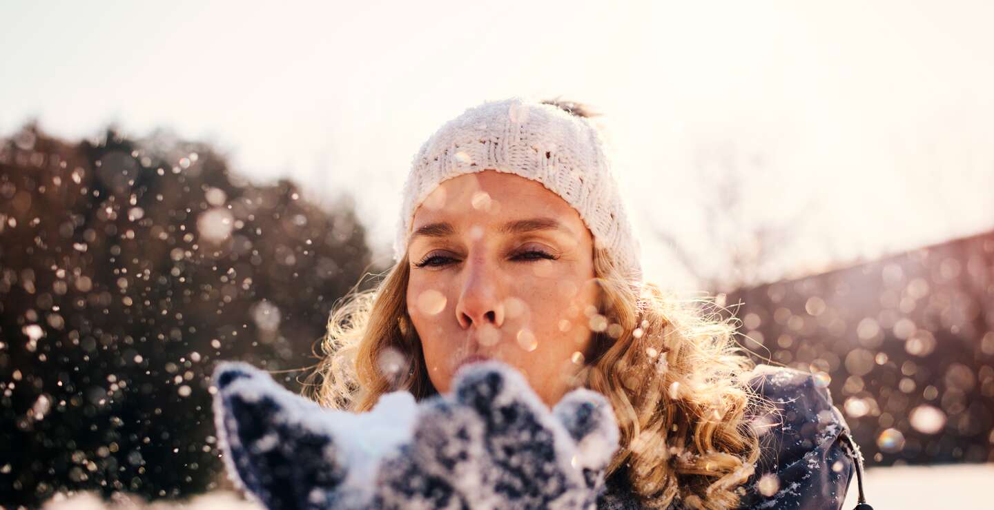 Frau im Freien im Winter pustet Schnee in die Luft | © Gettyimages.com/vgajic
