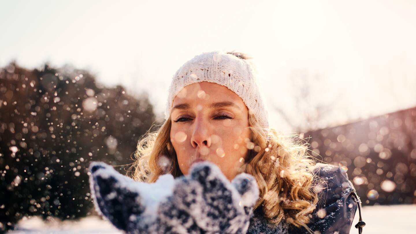 Frau im Freien im Winter pustet Schnee in die Luft | © Gettyimages.com/vgajic