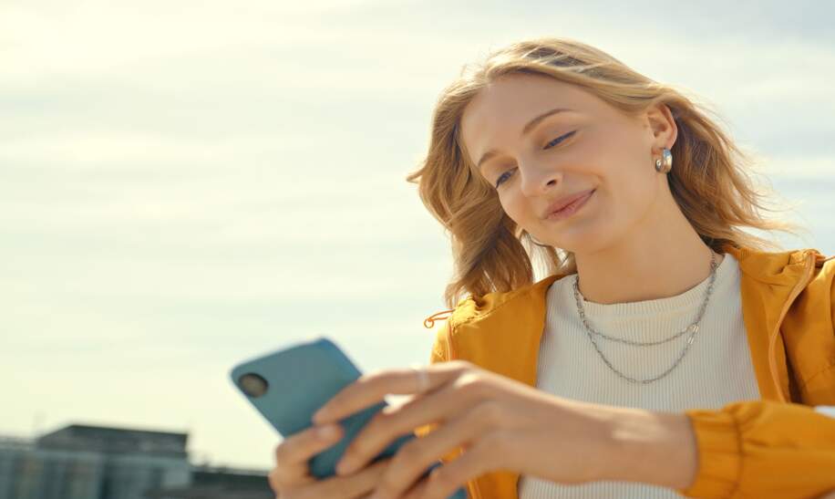 Frau sitzt auf einer Dachterrasse und schaut auf ihr Handy | © Gettyimages.com/marcovdm