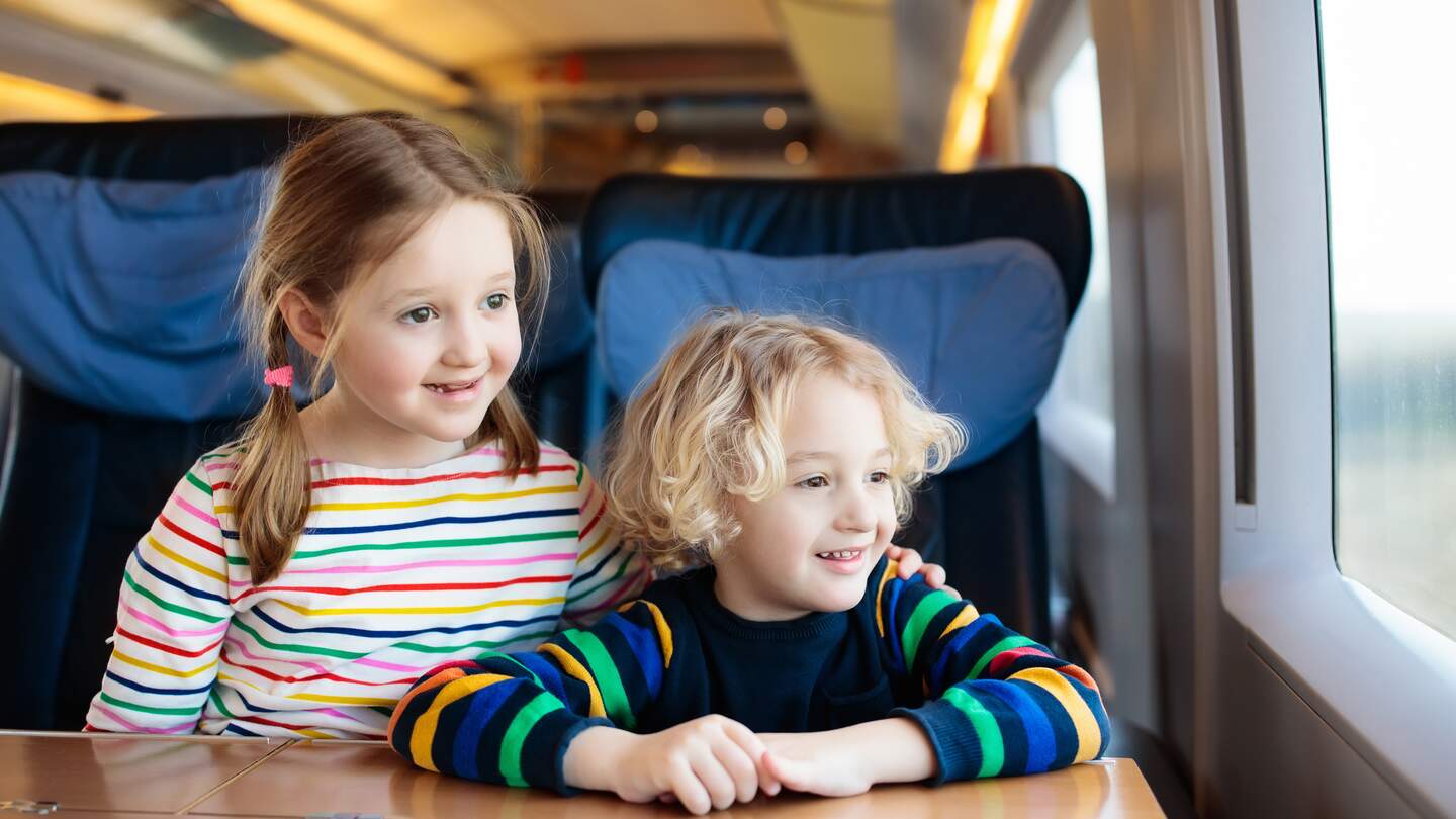 Zwei Kinder schauen aus dem Fenster währen sie mit der Bahn verreisen | © Gettyimages.com/FamVeld