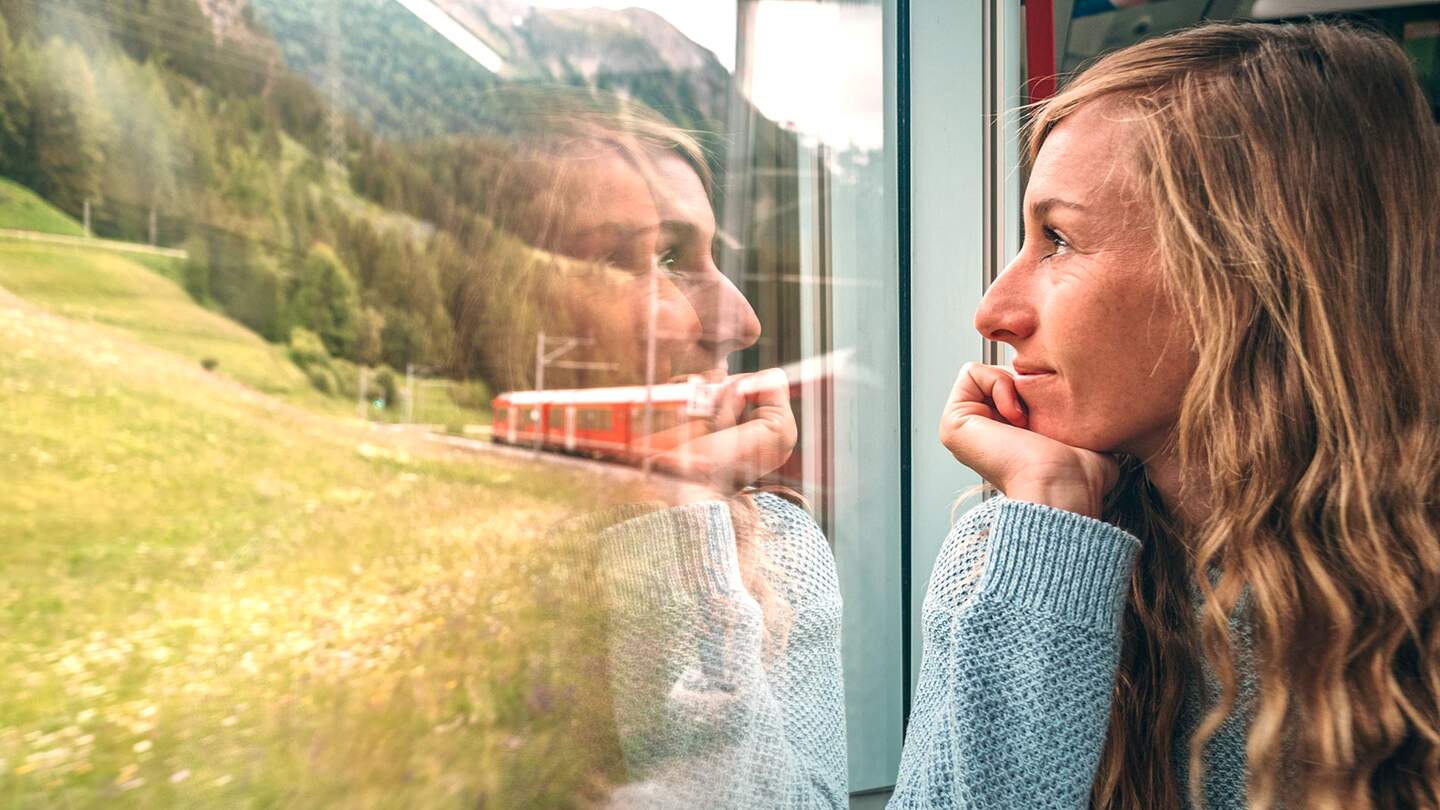 Frau, die mit dem Zug aus dem Fenster schaut und die landschaftlich vorbeifahrende Landschaft geniesst | © Gettyimages.com/Mystockimgaes